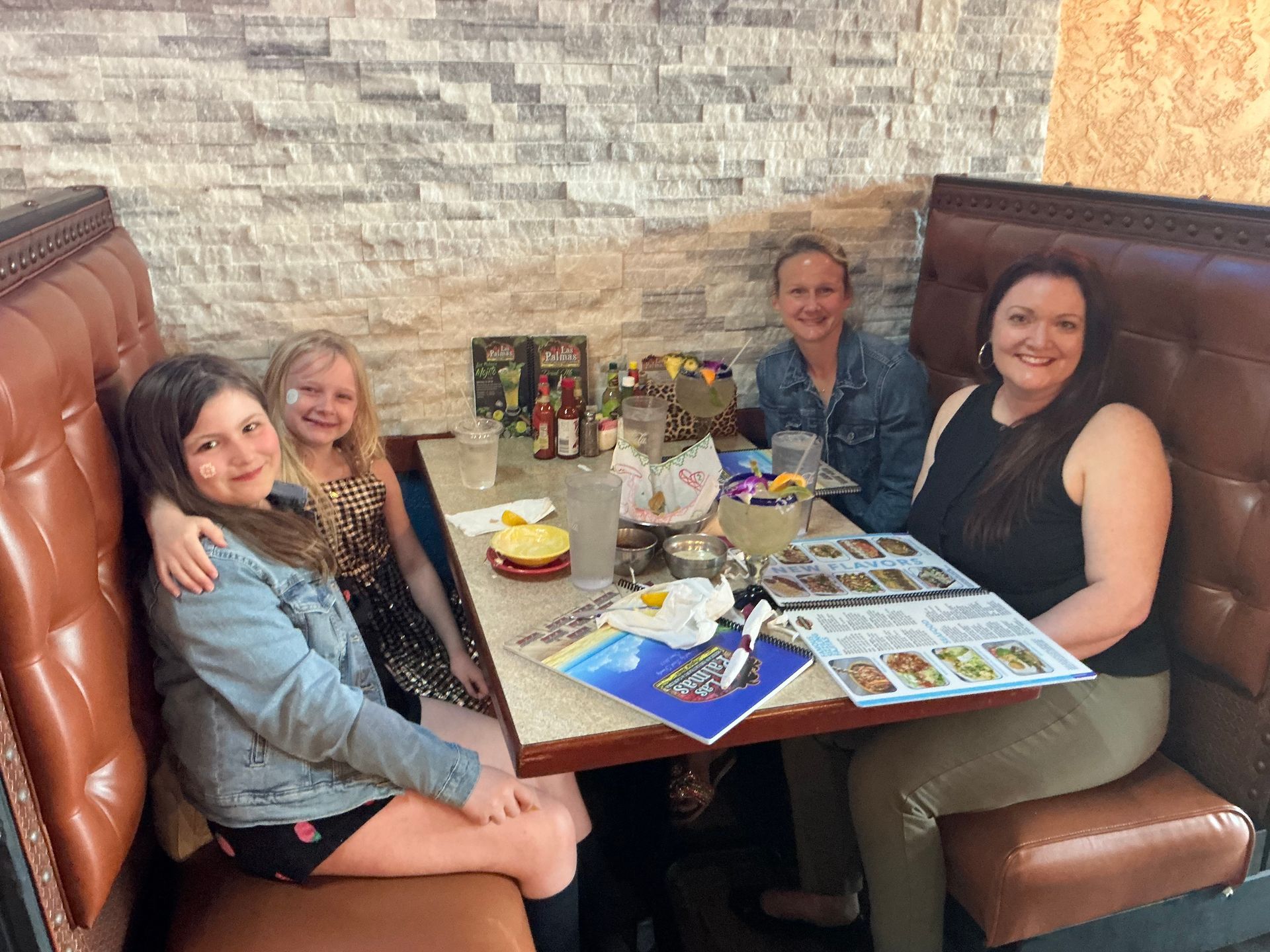 Four people seated at a table in a restaurant booth, looking at menus and smiling.