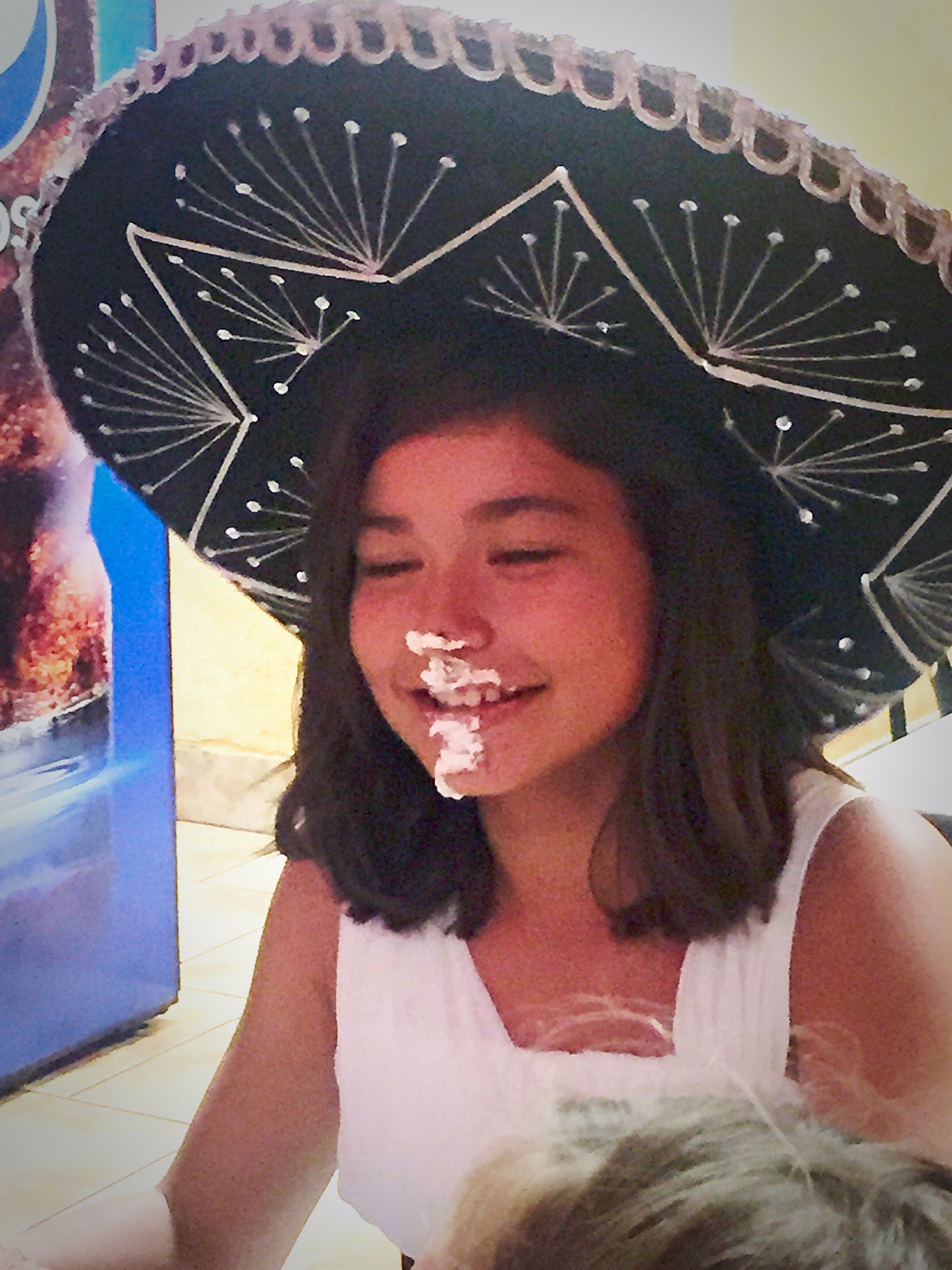 Person wearing a sombrero with whipped cream on their face, smiling.
