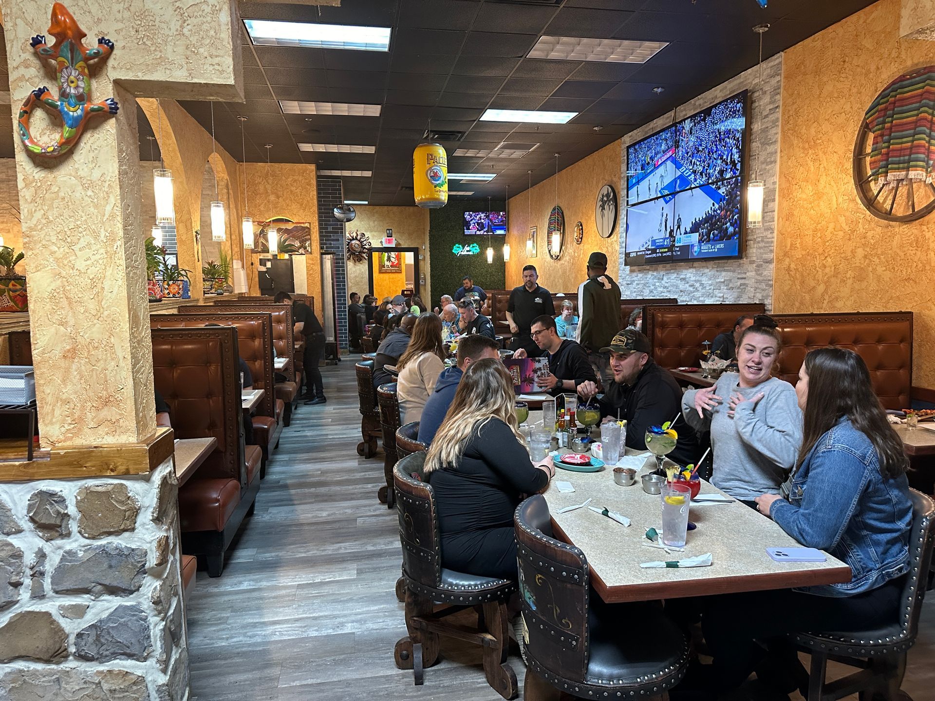 Interior of a Mexican restaurant with patrons seated at tables, some conversing. Decorations include a lizard and a hanging lantern.