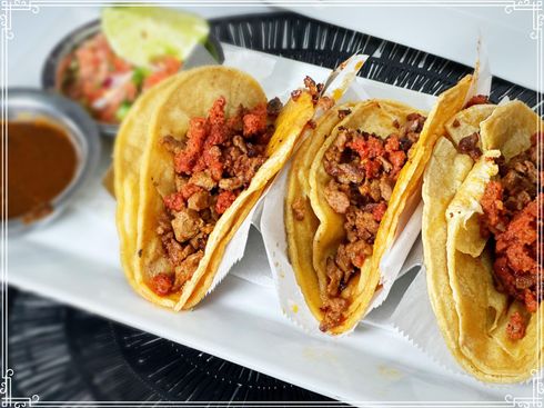 Three tacos with meat filling, served with salsa, lime, and sauce on a white plate.
