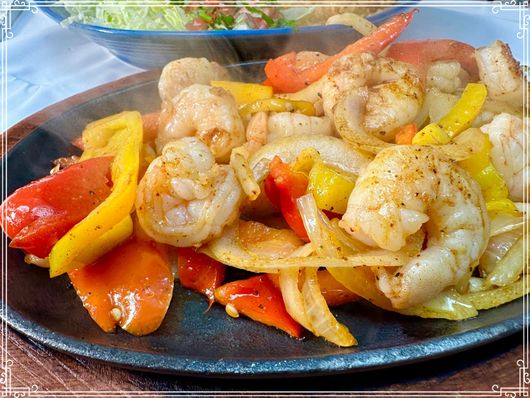 Sizzling plate of shrimp, scallops, and bell peppers with a side salad.