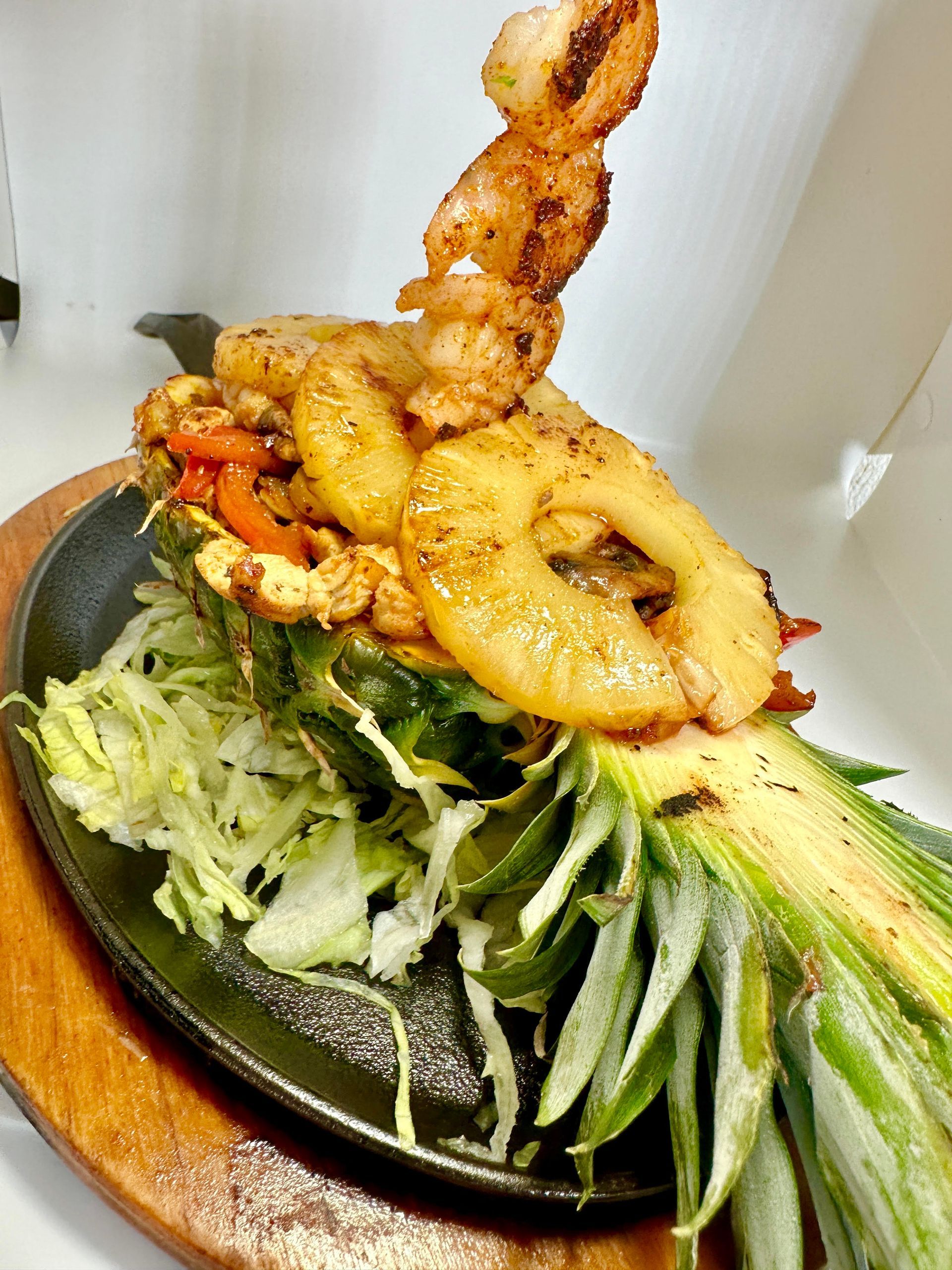 Shrimp fajita in pineapple shell, on a sizzling platter with lettuce, wood base.