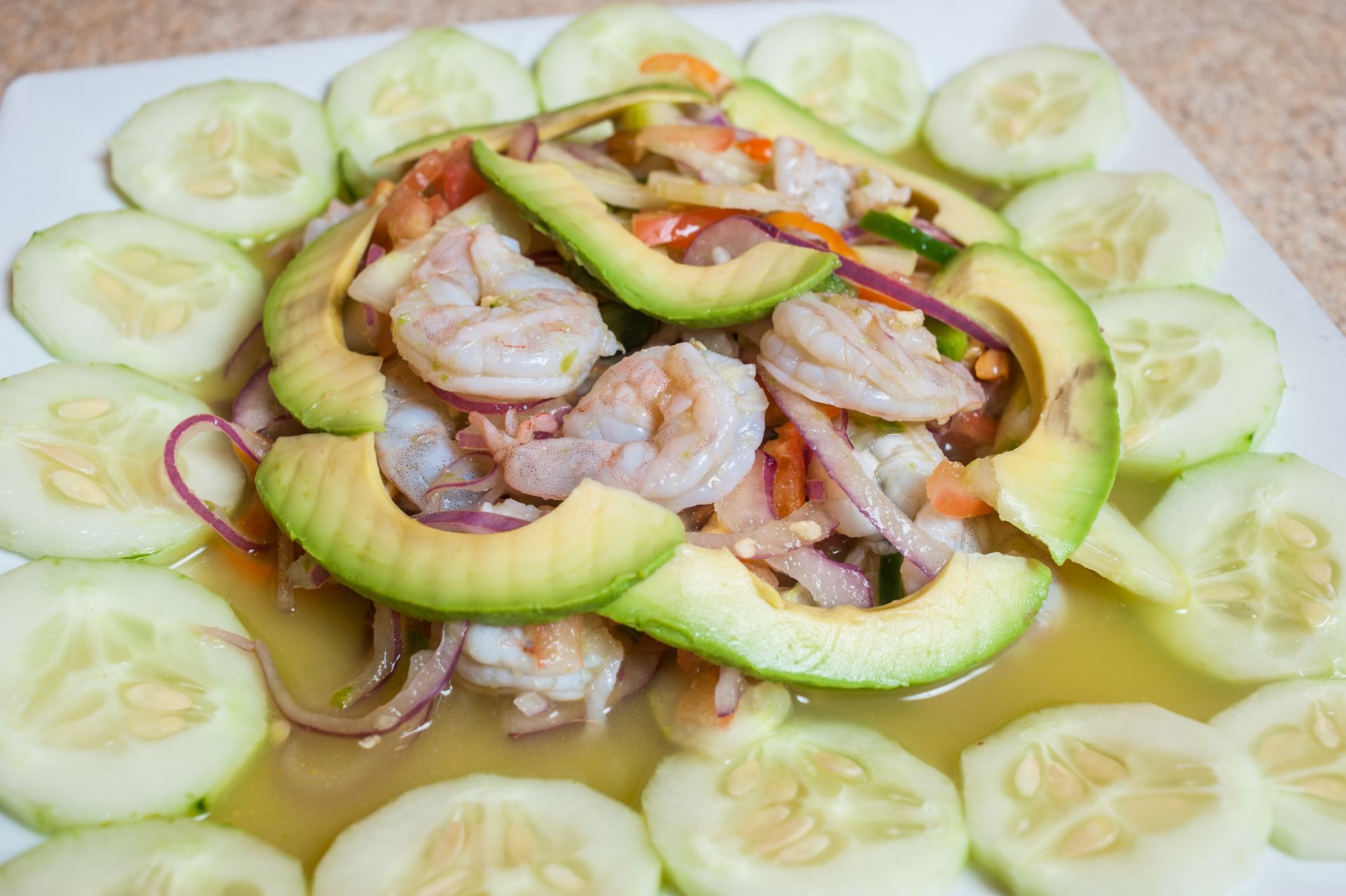 Shrimp ceviche with avocado and cucumber slices on a white plate.