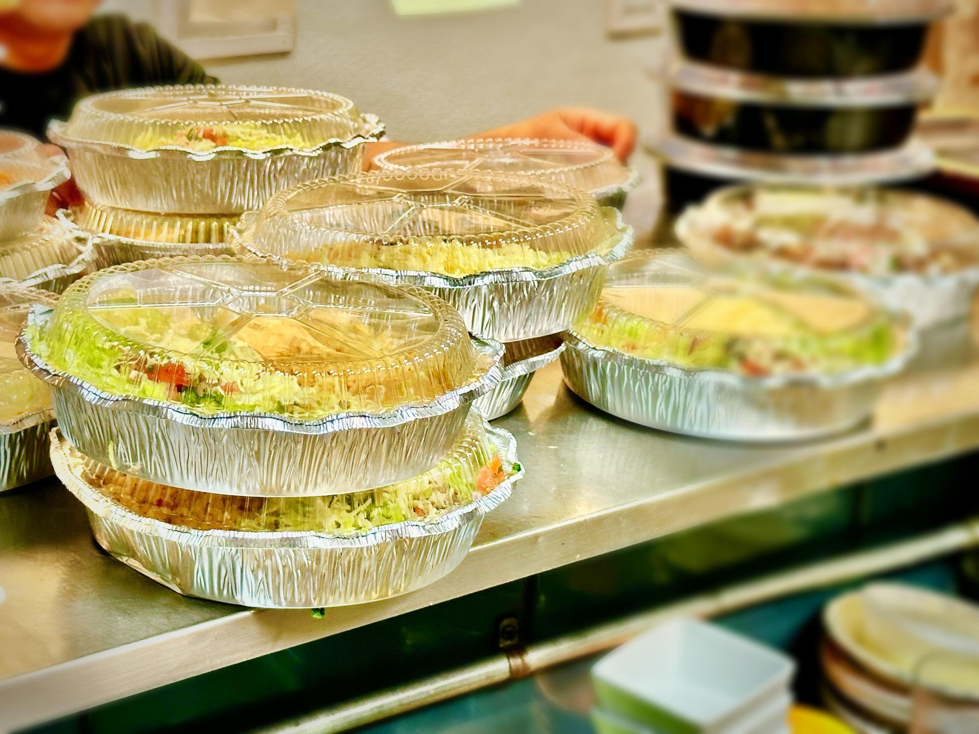 Aluminum containers of food, stacked and arranged on a metal counter, ready for takeout.
