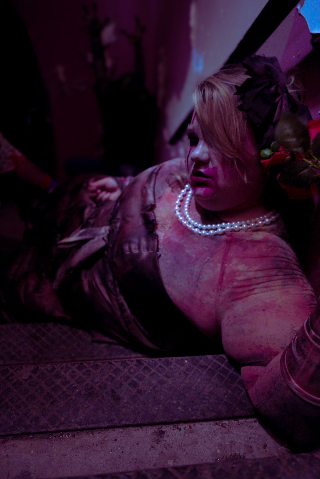 Woman in gown, pearl necklace, reclined on steps, dimly lit.