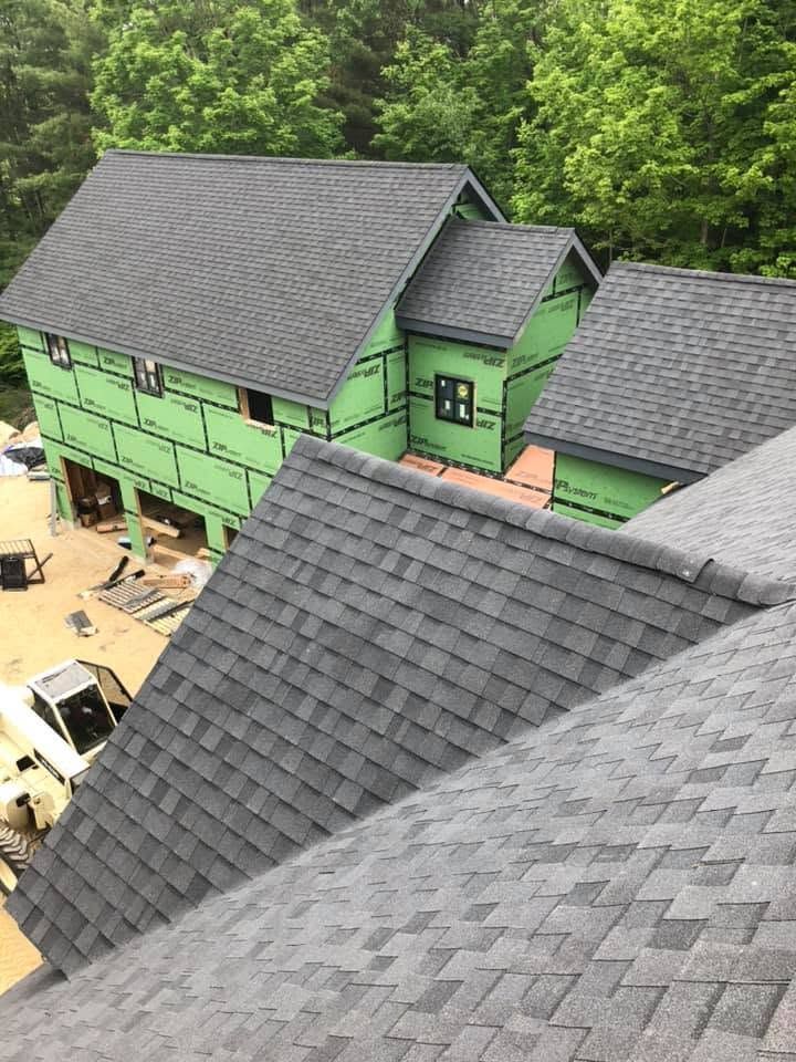 Partially built houses with green sheathing and dark gray shingles in a wooded area Partially built houses with green sheathing and dark gray shingles in a wooded area