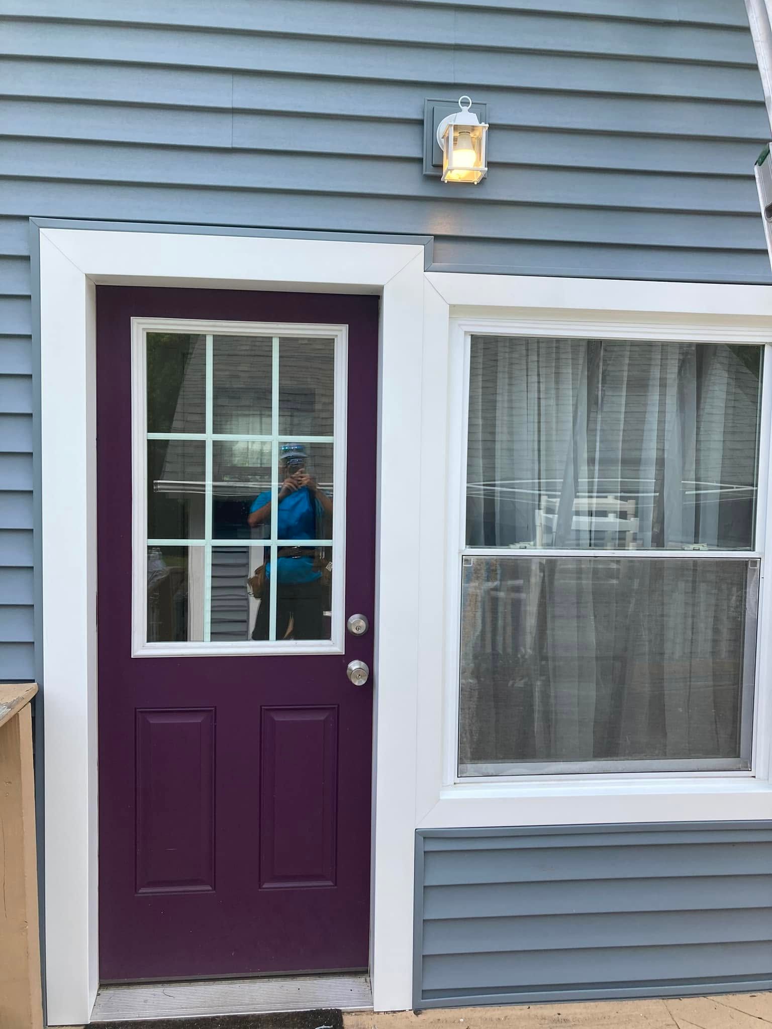 Purple front door beside a window on a blue house with white trim and a porch light above Purple front door beside a window on a blue house with white trim and a porch light above