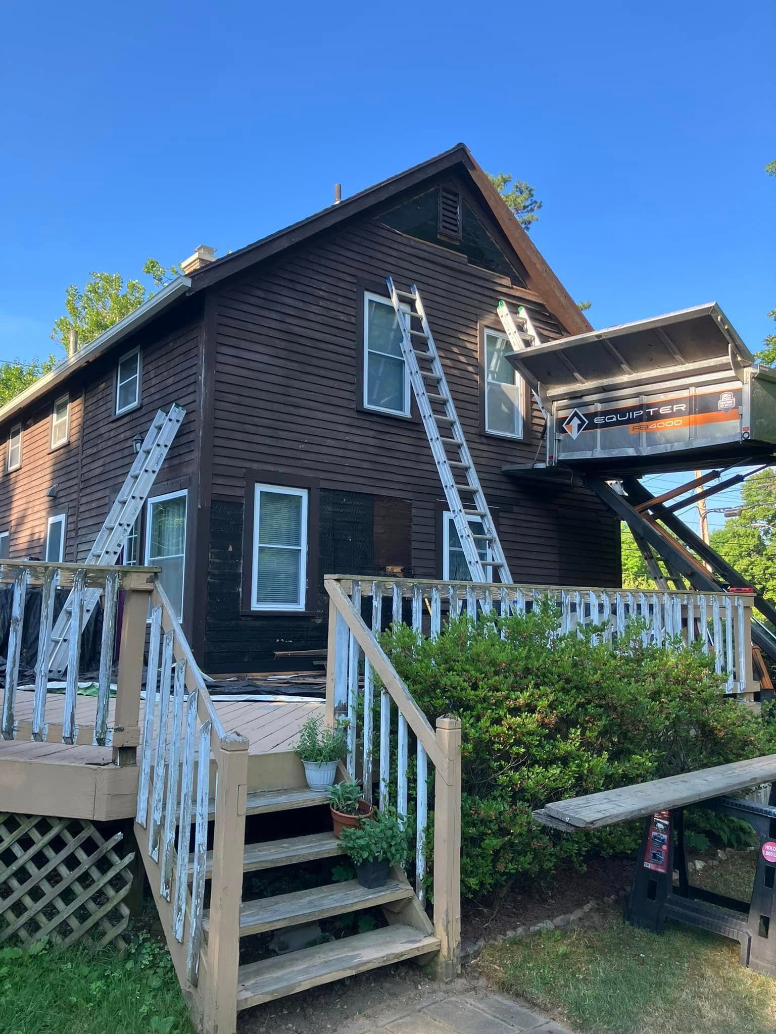 Dark brown house with white trim, front stairs, porch railing, and raised deck against a blue sky Dark brown house with white trim, front stairs, porch railing, and raised deck against a blue sky