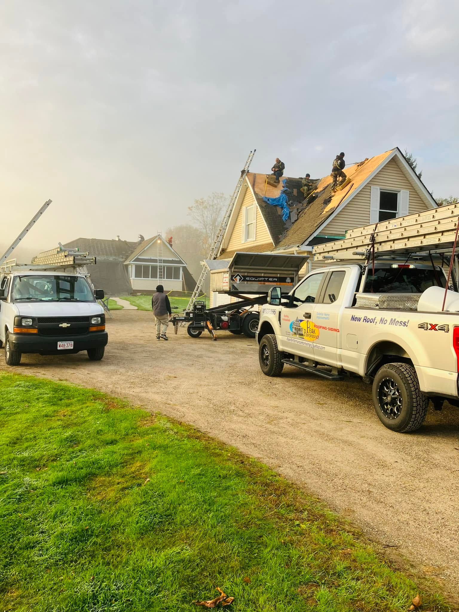 Workers and trucks at a storm-damaged house with a torn roof and debris in the driveway Workers and trucks at a storm-damaged house with a torn roof and debris in the driveway