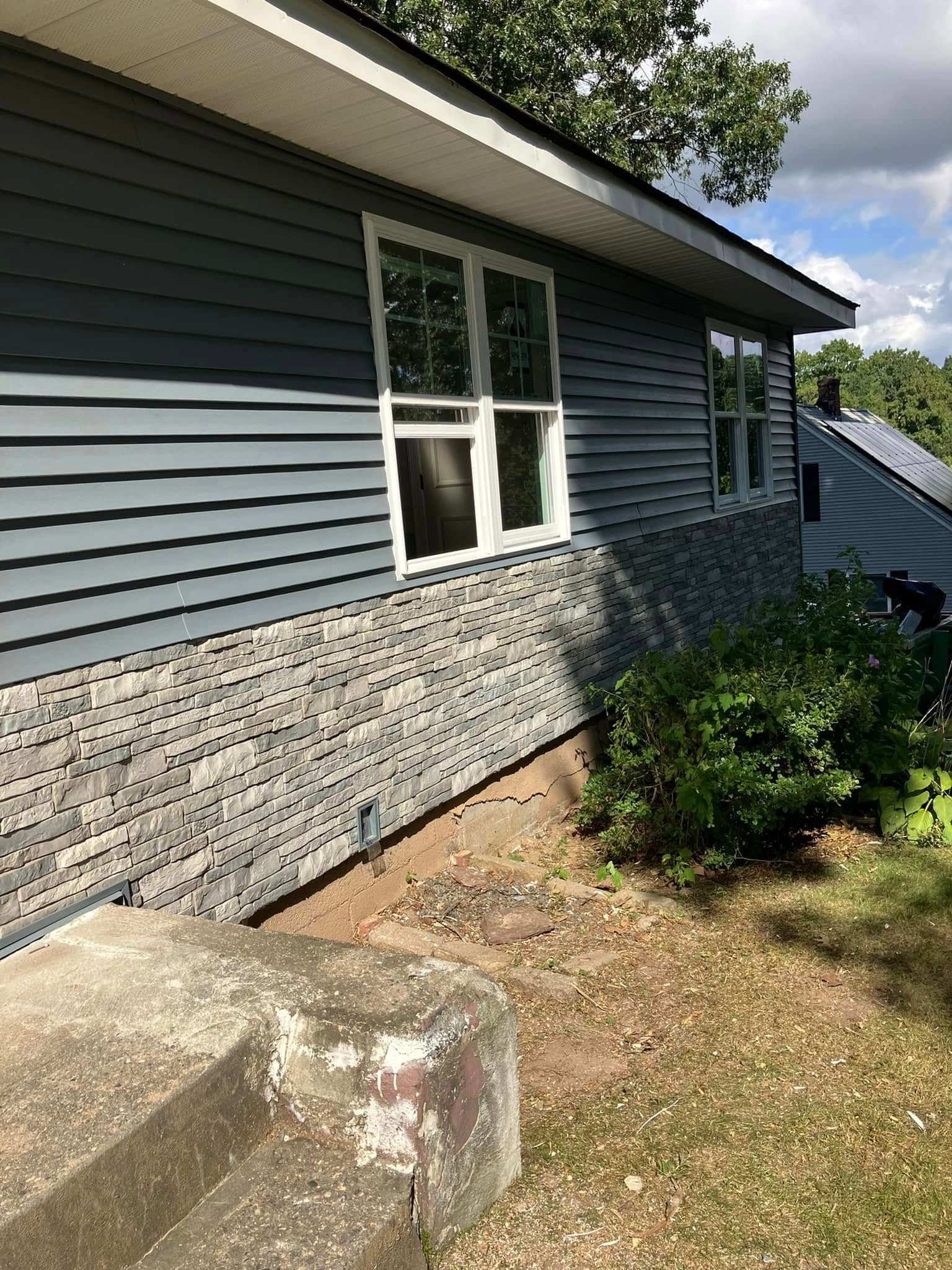 Blue-gray house exterior with white-trimmed window, stone foundation, and steps beside a sloped yard Blue-gray house exterior with white-trimmed window, stone foundation, and steps beside a sloped yard
