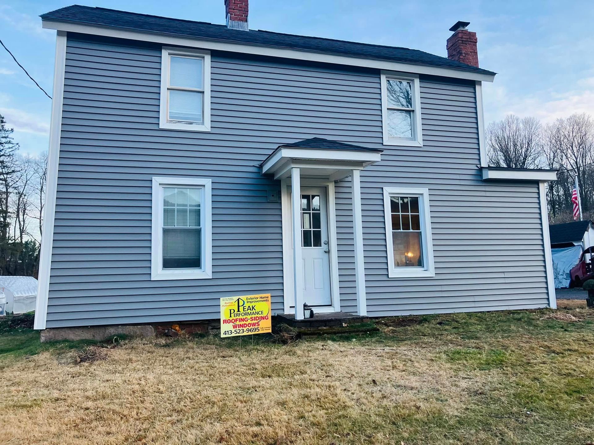 Gray two-story house with white trim and a small front porch, with a yard sign in the front lawn. Gray two-story house with white trim and a small front porch, with a yard sign in the front lawn.