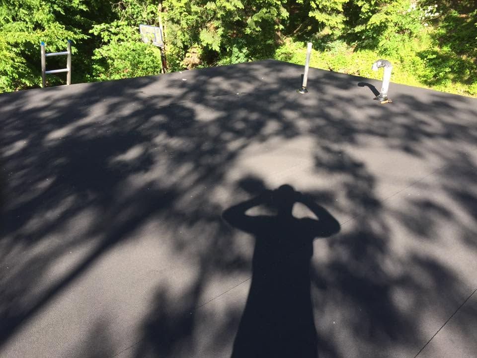 Shaded rooftop with trees in the background and a person’s shadow in the foreground Shaded rooftop with trees in the background and a person’s shadow in the foreground