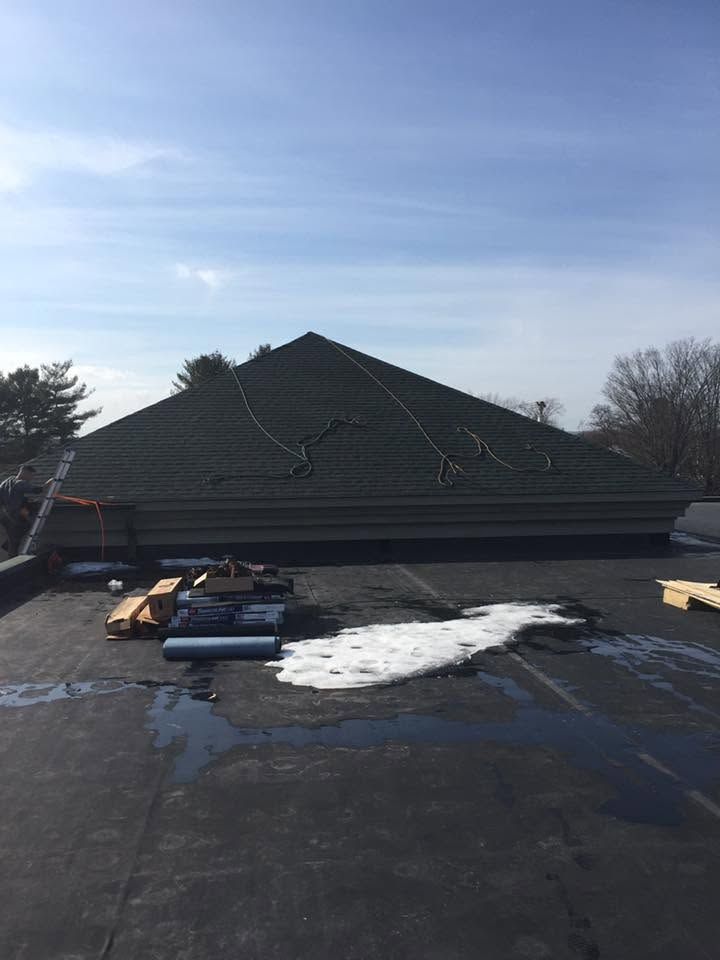 Snow-dusted dark roof with patches of snow and a cloudy blue sky overhead Snow-dusted dark roof with patches of snow and a cloudy blue sky overhead
