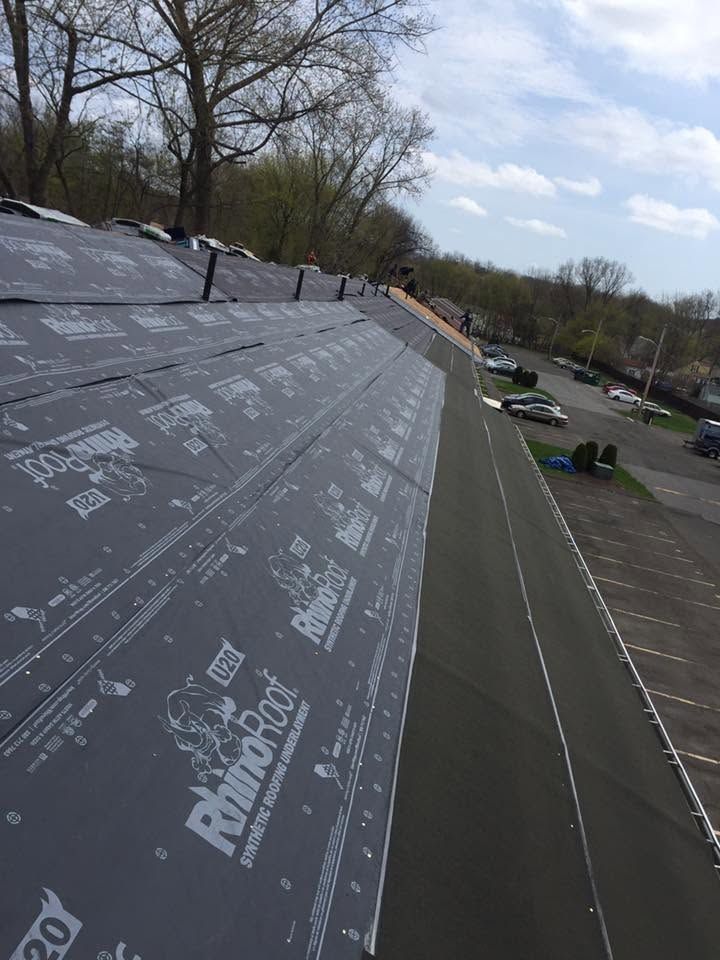 Roof under construction with underlayment being installed, viewed beside a parking lot and trees. Roof under construction with underlayment being installed, viewed beside a parking lot and trees.