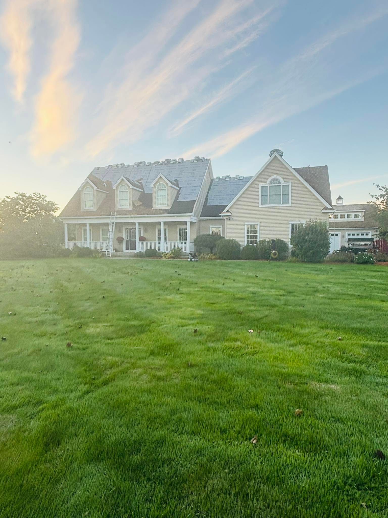 Large beige house with a gray roof and a wide green lawn under a bright sunset sky Large beige house with a gray roof and a wide green lawn under a bright sunset sky