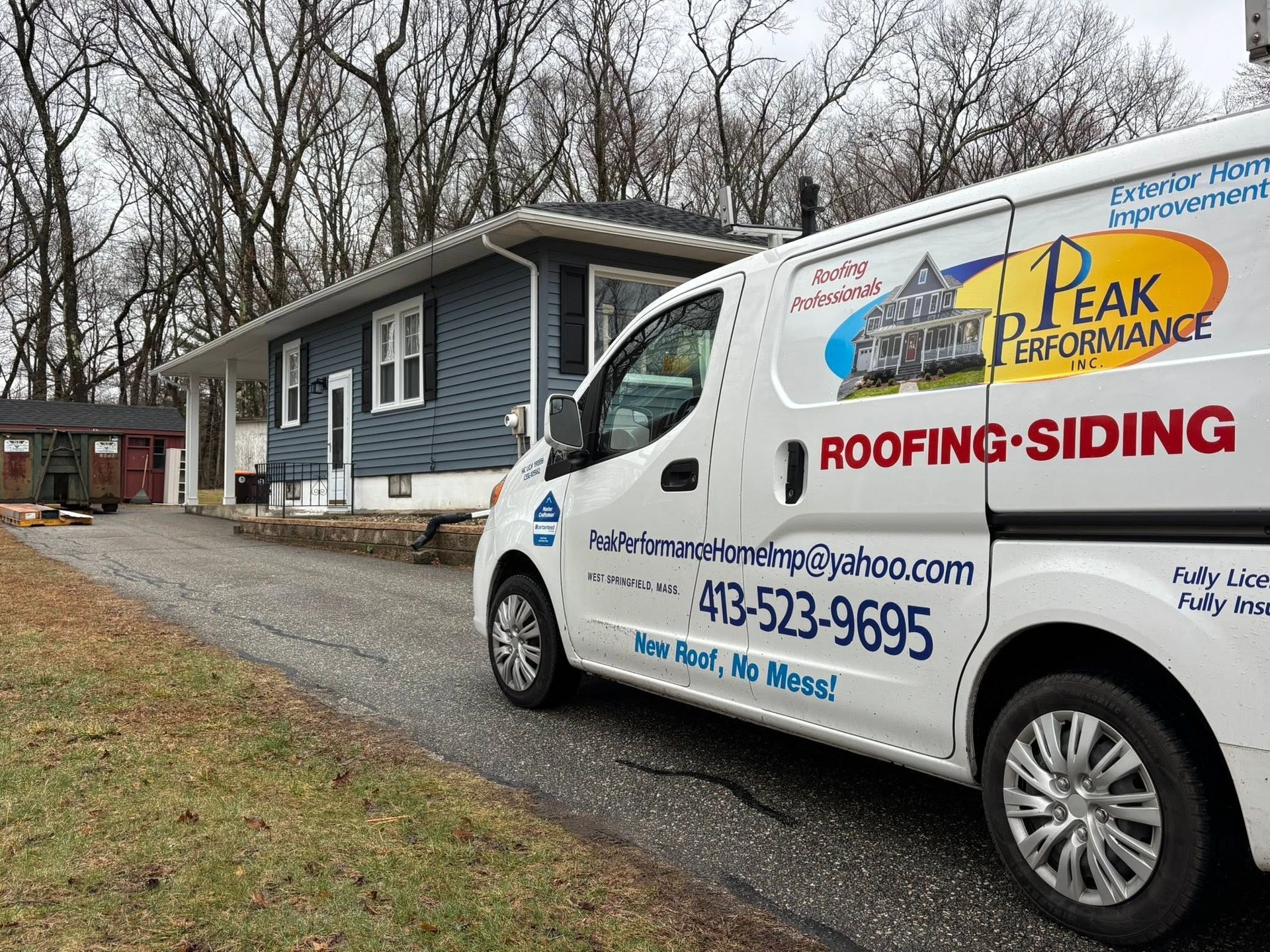 White roofing-siding van parked beside a blue house with business logos on a cloudy day