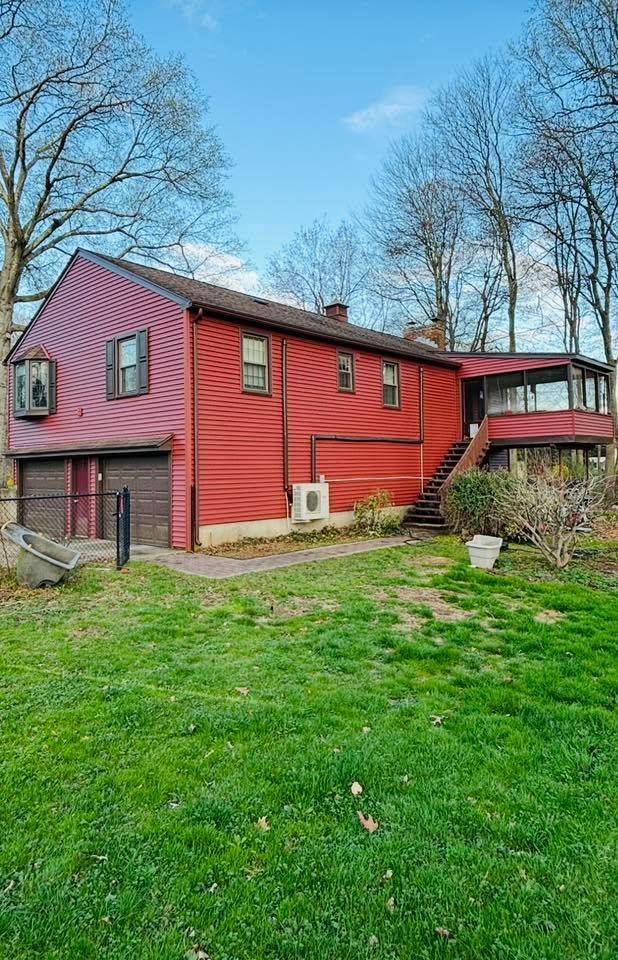 Red two-story house with a metal roof in a grassy yard, surrounded by bare trees and blue sky Red two-story house with a metal roof in a grassy yard, surrounded by bare trees and blue sky