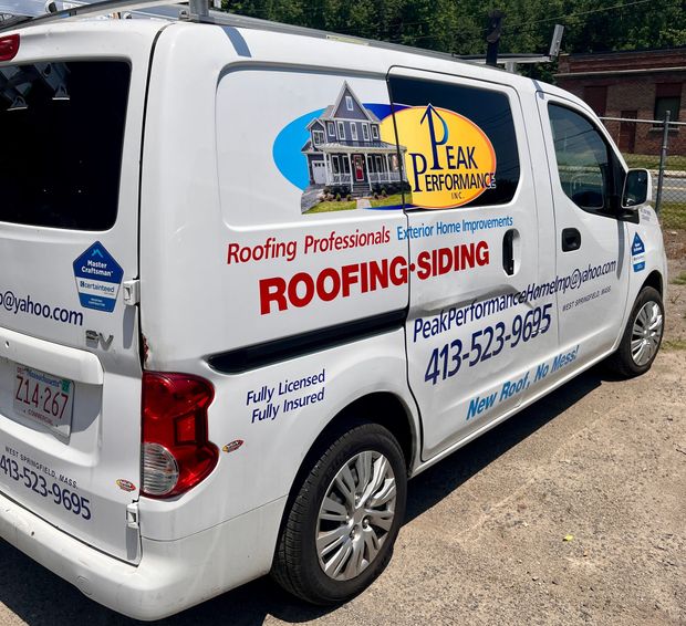 White roofing and siding van with company logos and phone number parked outdoors at a job site White roofing and siding van with company logos and phone number parked outdoors at a job site