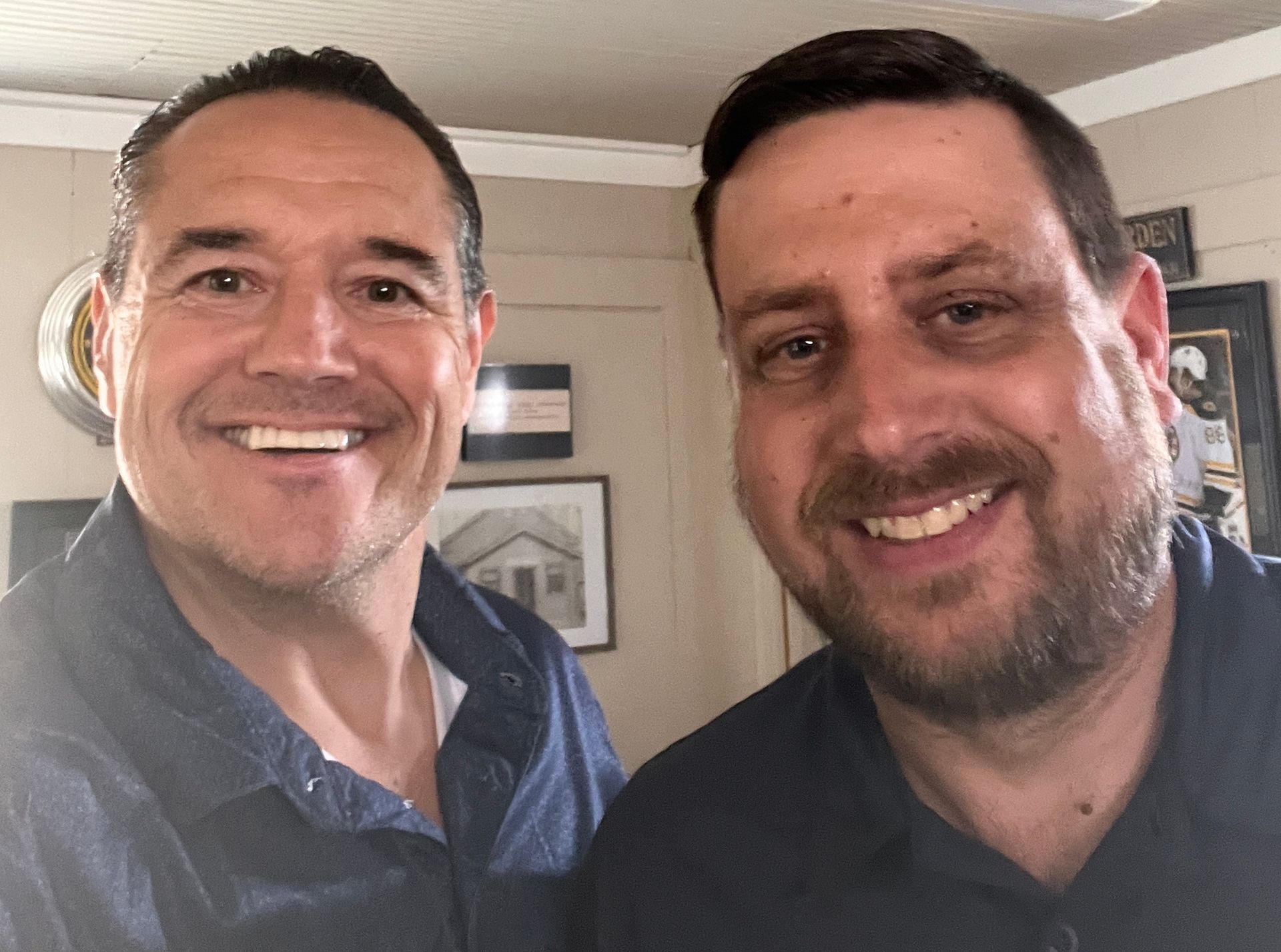 Two smiling men posing indoors, one in a blue shirt and one in a dark shirt.