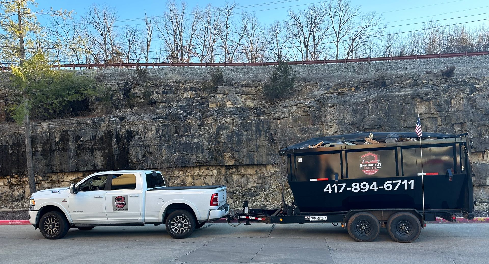 A white truck with a trailer attached to it is parked in front of a stone wall.