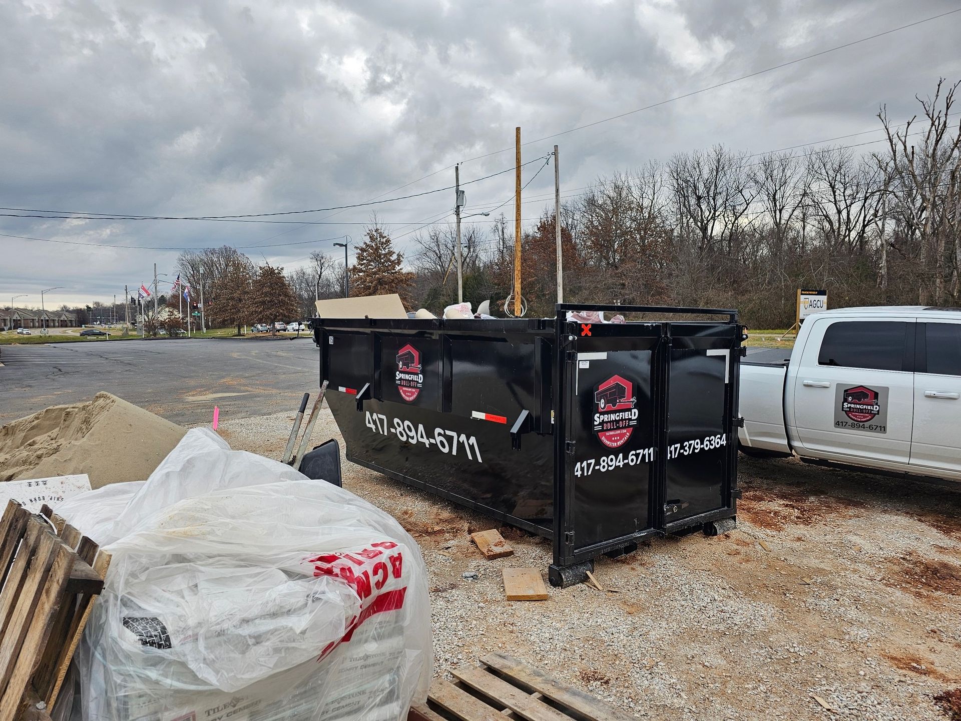 A dumpster is sitting in a parking lot next to a truck.