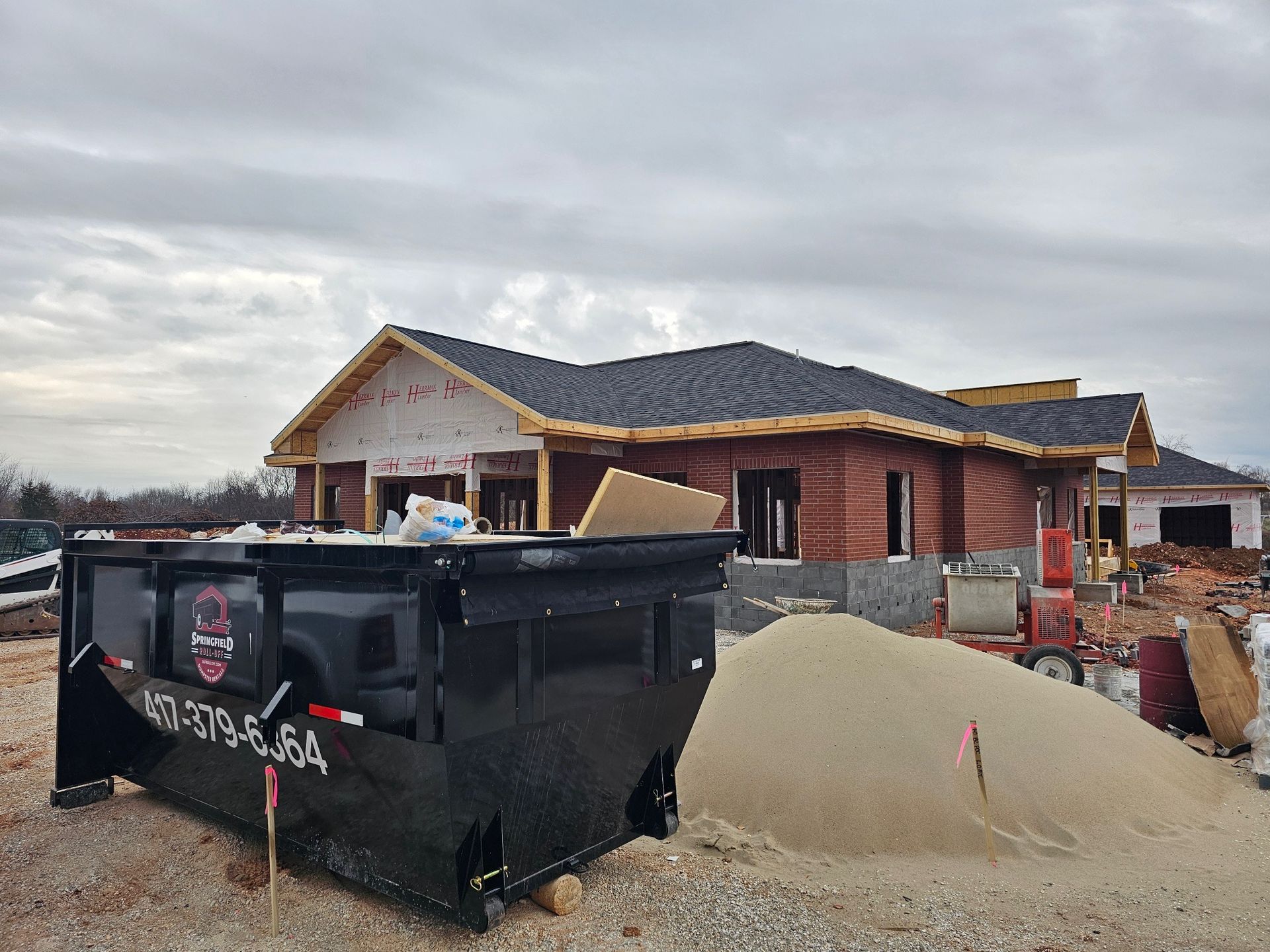 A dumpster is sitting in front of a house under construction.