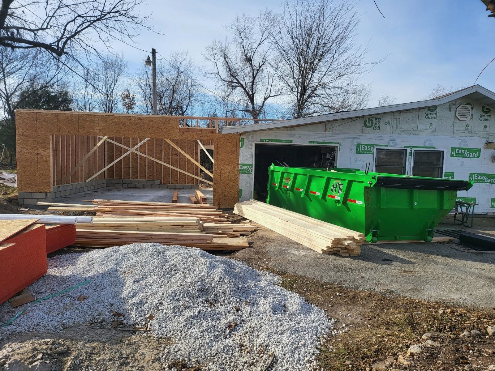 A green dumpster is sitting in front of a house under construction.