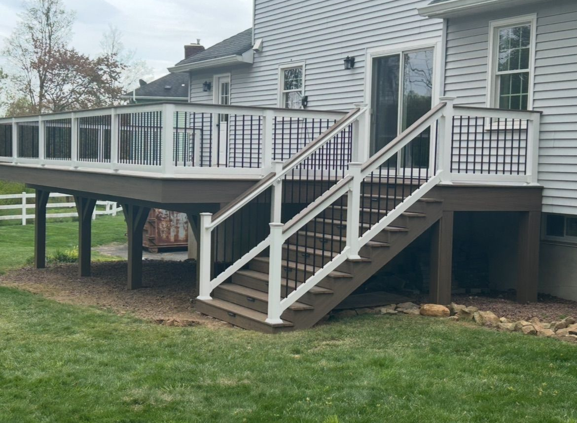 Raised wooden deck with white railings and stairs beside a house over a grassy yard