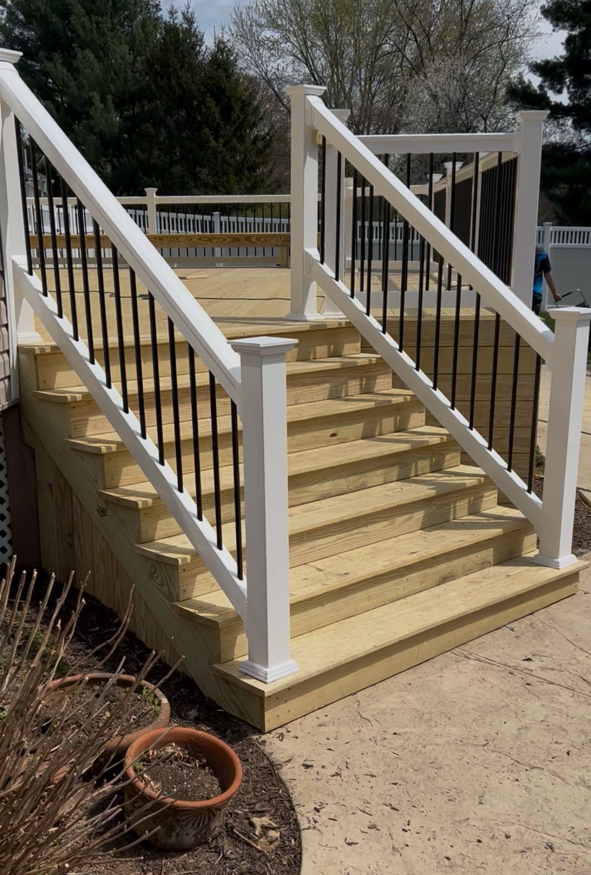 Wooden outdoor staircase with white railings and black balusters leading up to a deck.