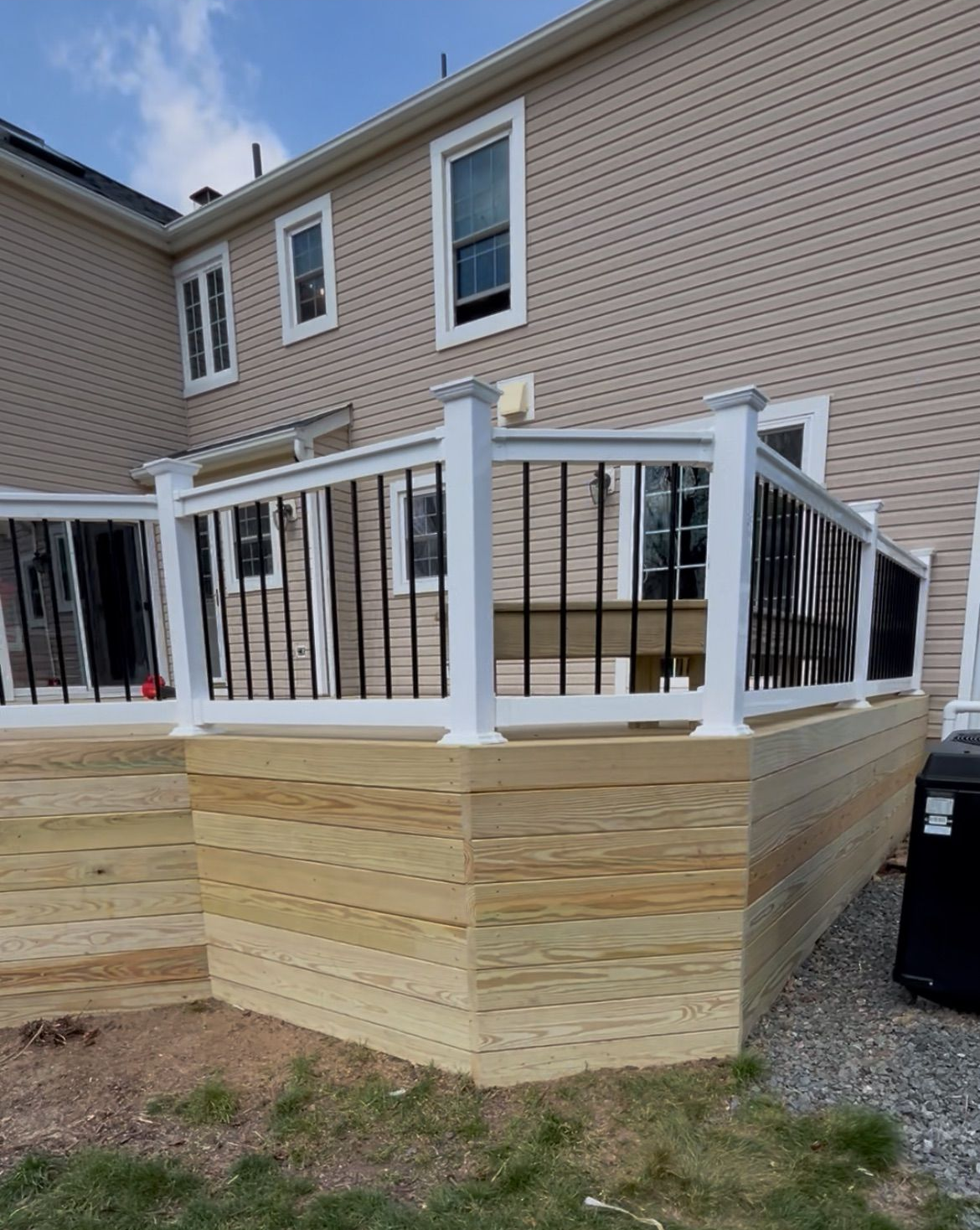 Deck with white railing and black balusters beside a tan house