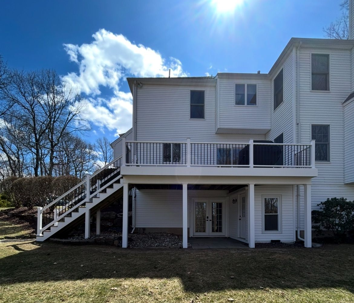 White two-story house with an exterior staircase and deck under a bright blue sky