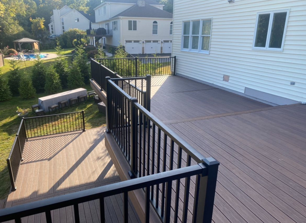 Back deck with black railing and brown flooring beside a white house, overlooking a small yard and neighboring homes