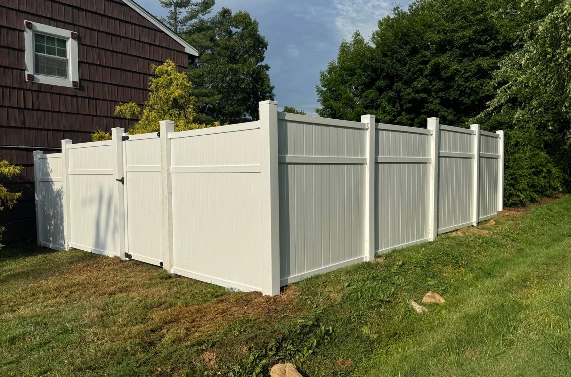 White vinyl privacy fence around a yard beside a house on a grassy slope
