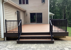 Wooden deck with black railings and steps leading to a beige house patio door