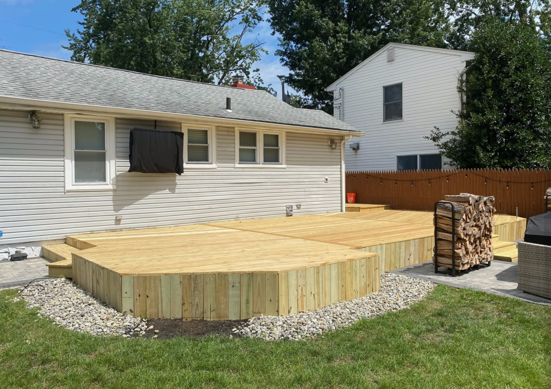 Backyard wooden deck with curved steps beside a house, bordered by gravel and grass