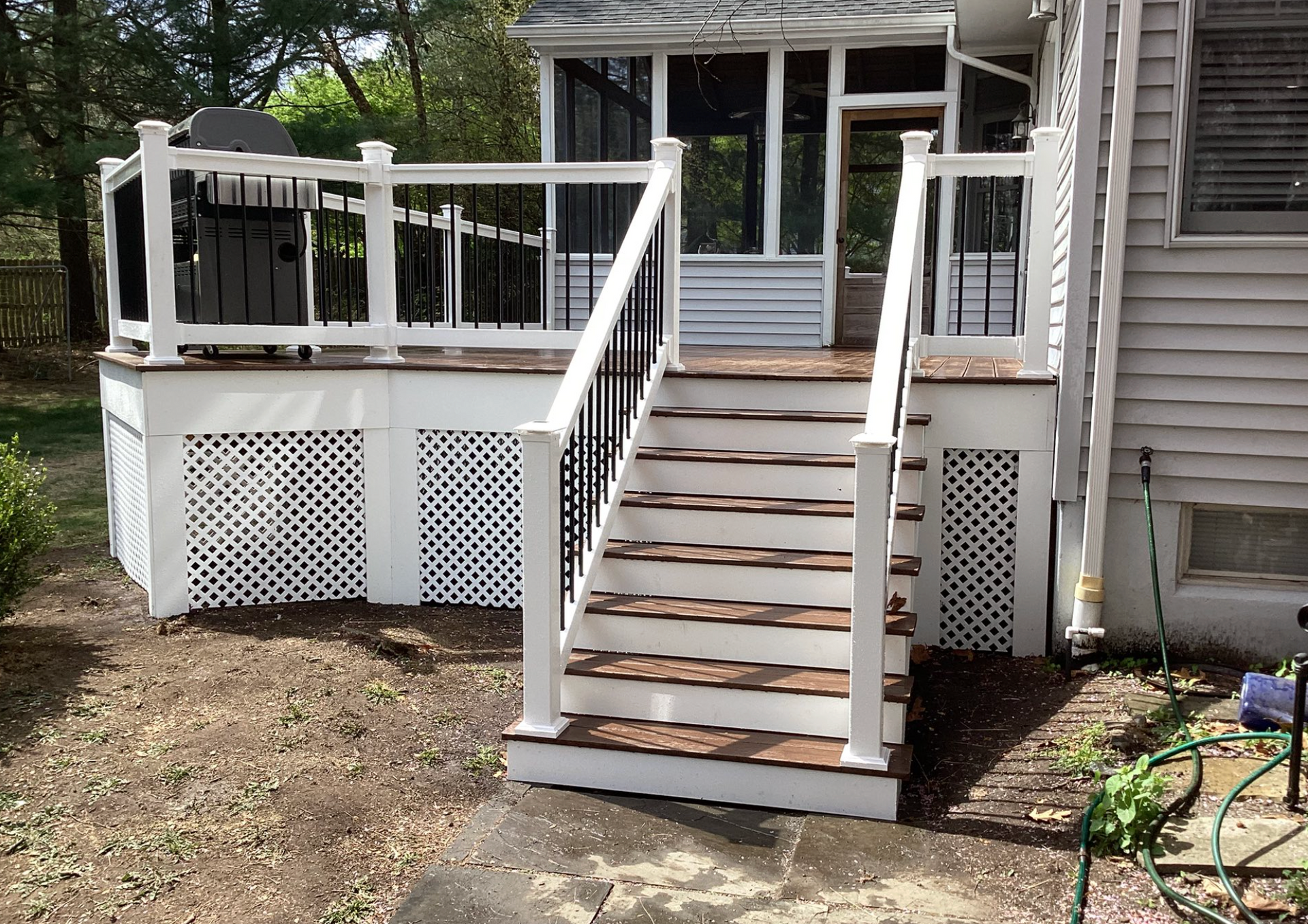 White front porch with stairs and railings leading to a house entrance, surrounded by gravel and lattice skirting