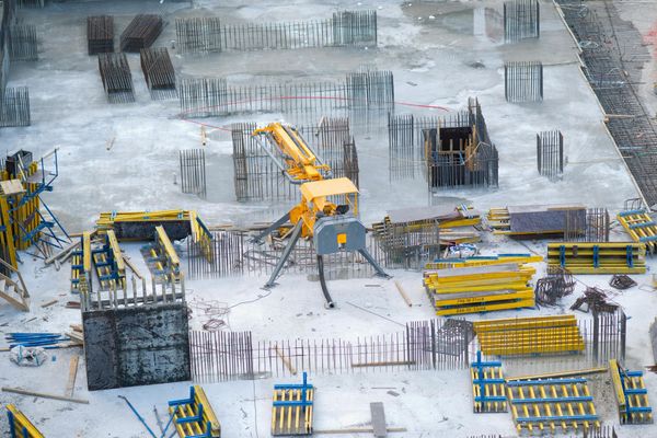 Construction site with yellow excavator and steel rebar frames on a snowy ground