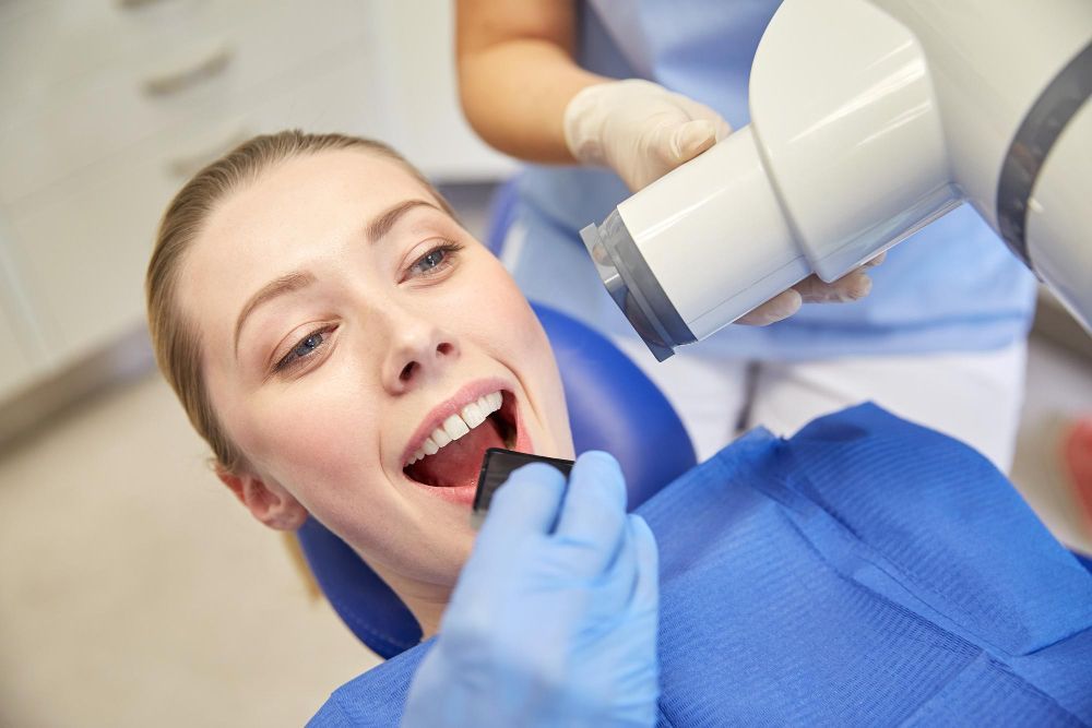Woman getting dental X-ray. Dentist in blue gloves and uniform. Clinic setting.