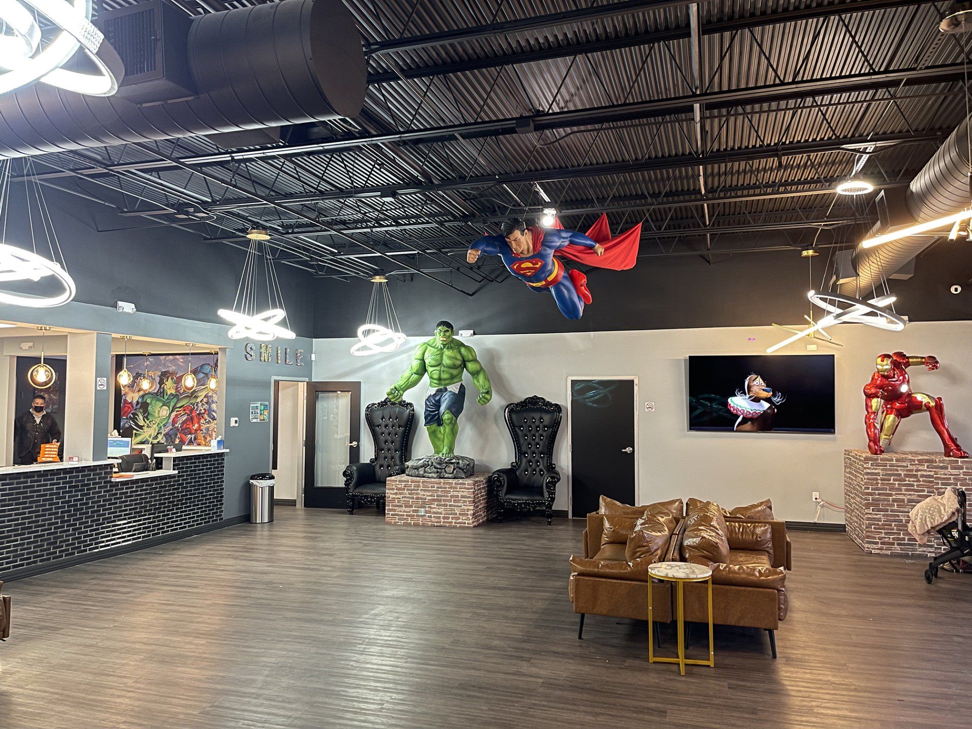Superhero-themed lobby with large wall art, statues, and a brown couch on a glossy floor