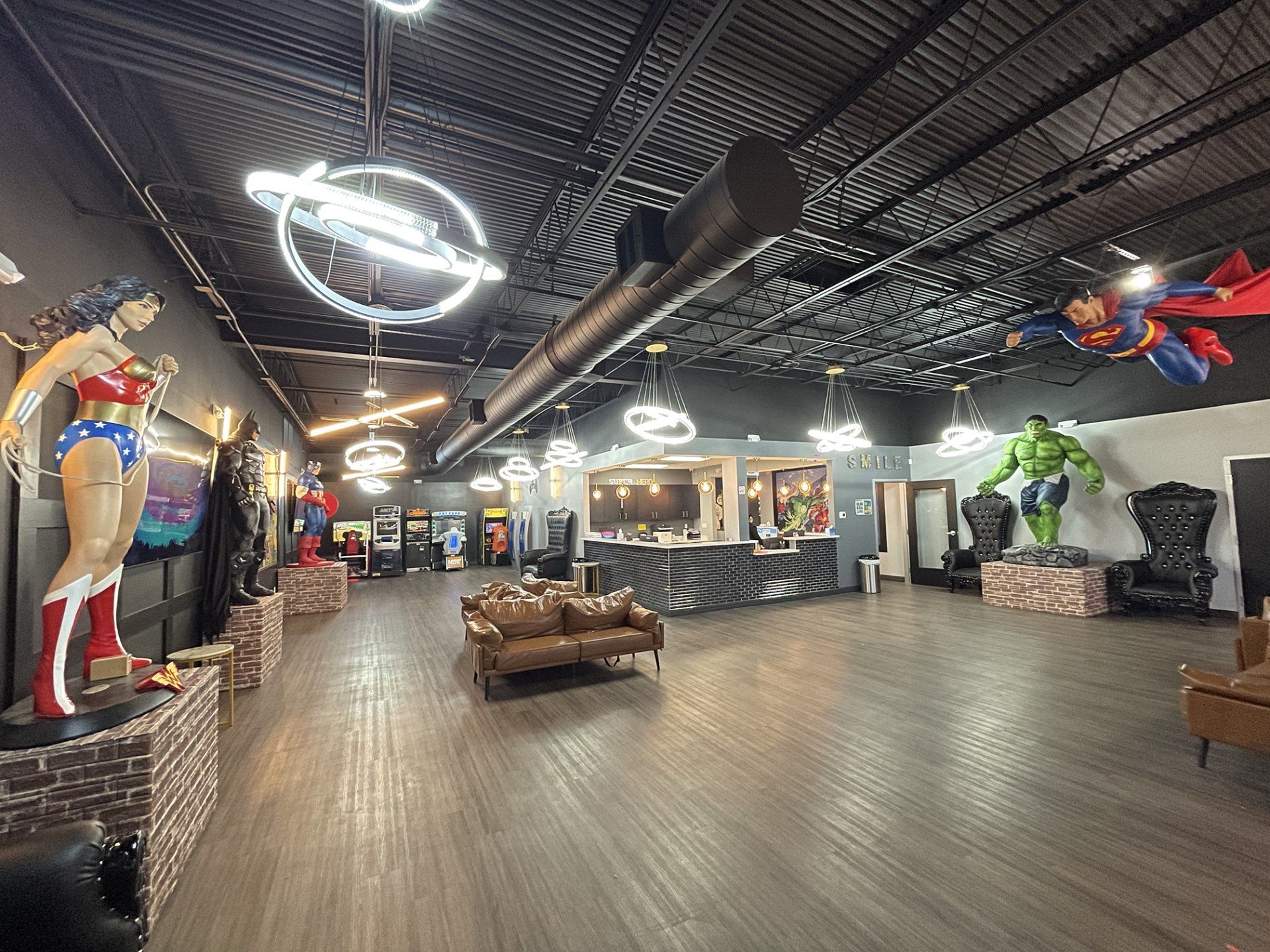 Interior of a superhero-themed lobby with statues, neon signs, and seating under a dark ceiling