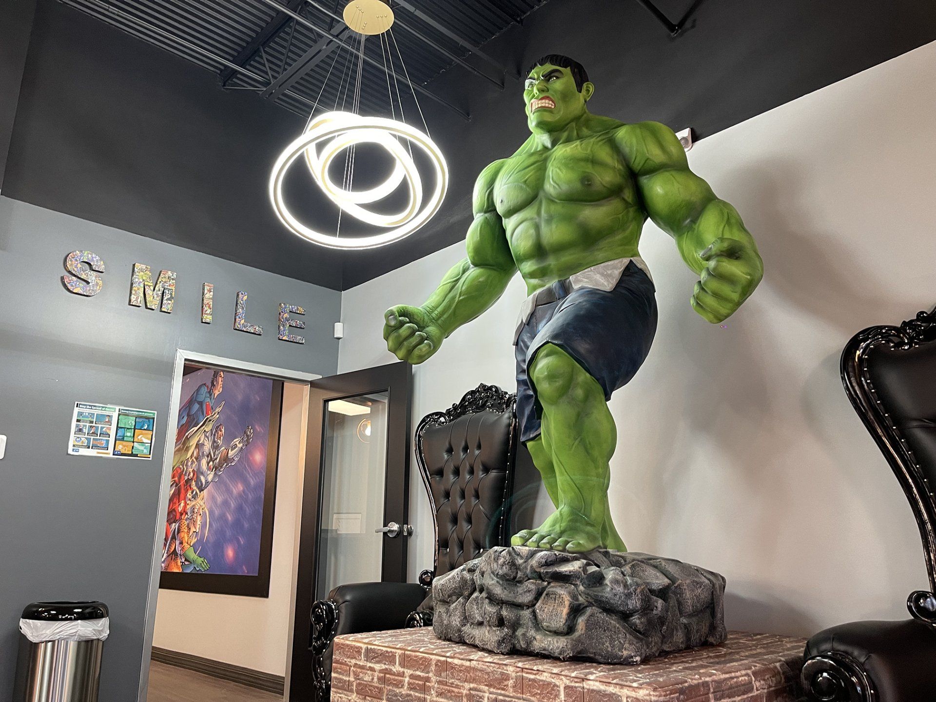 Large green Hulk statue standing on a rock base in a modern indoor lobby with a ceiling light and wall art.