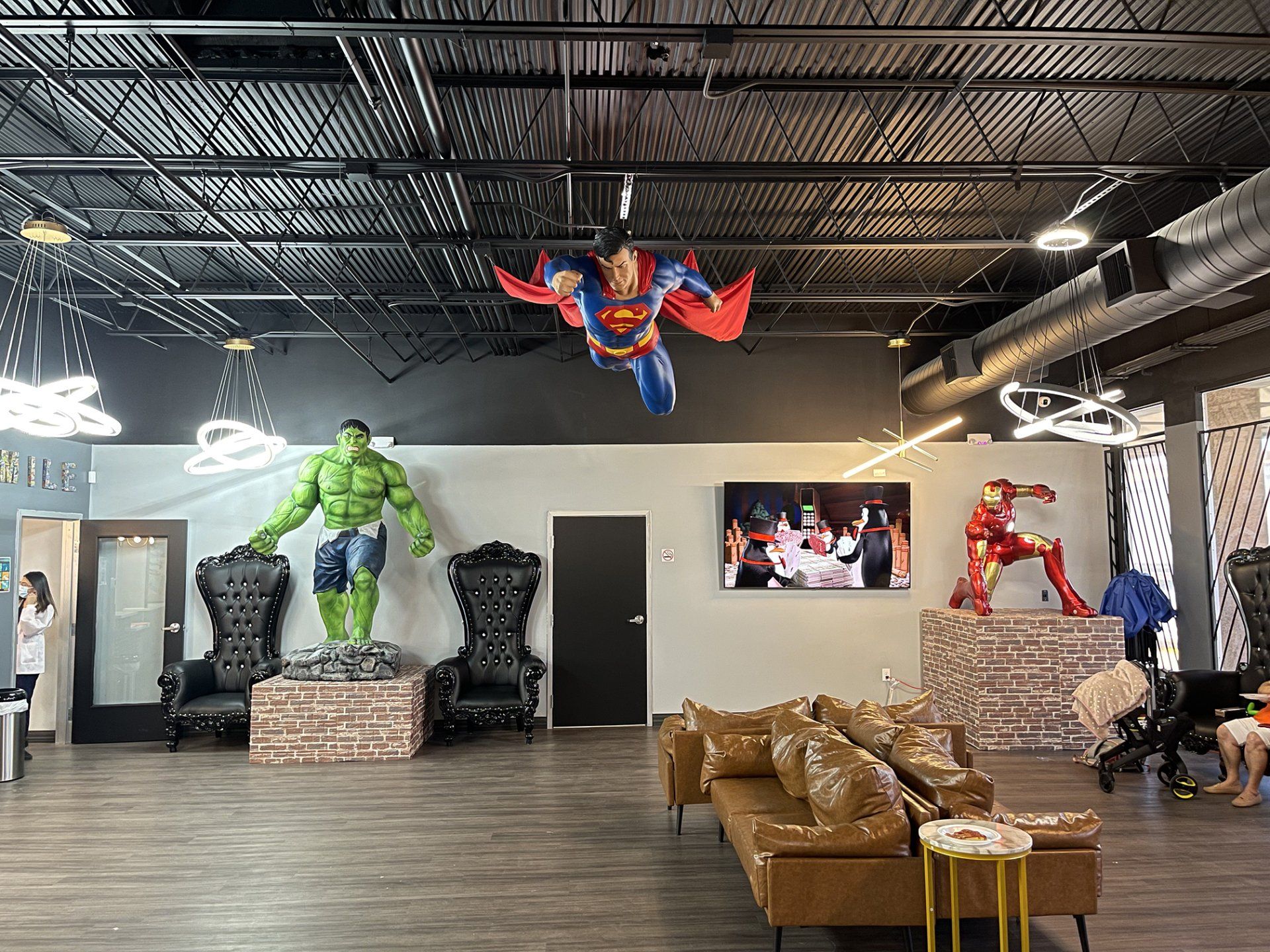 Superhero-themed lounge with Hulk, Spider-Man, and Iron Man statues around brown chairs and a TV