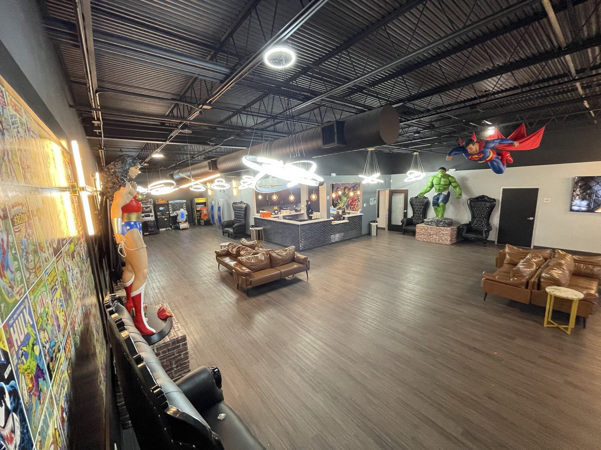 Wide indoor lounge with wood floors, tables, couches, and colorful wall murals under an exposed black ceiling.