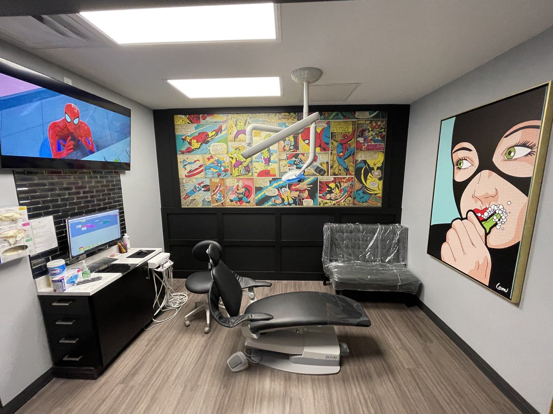 Bright studio office with dual monitors, exercise bench, couch, and colorful wall art.