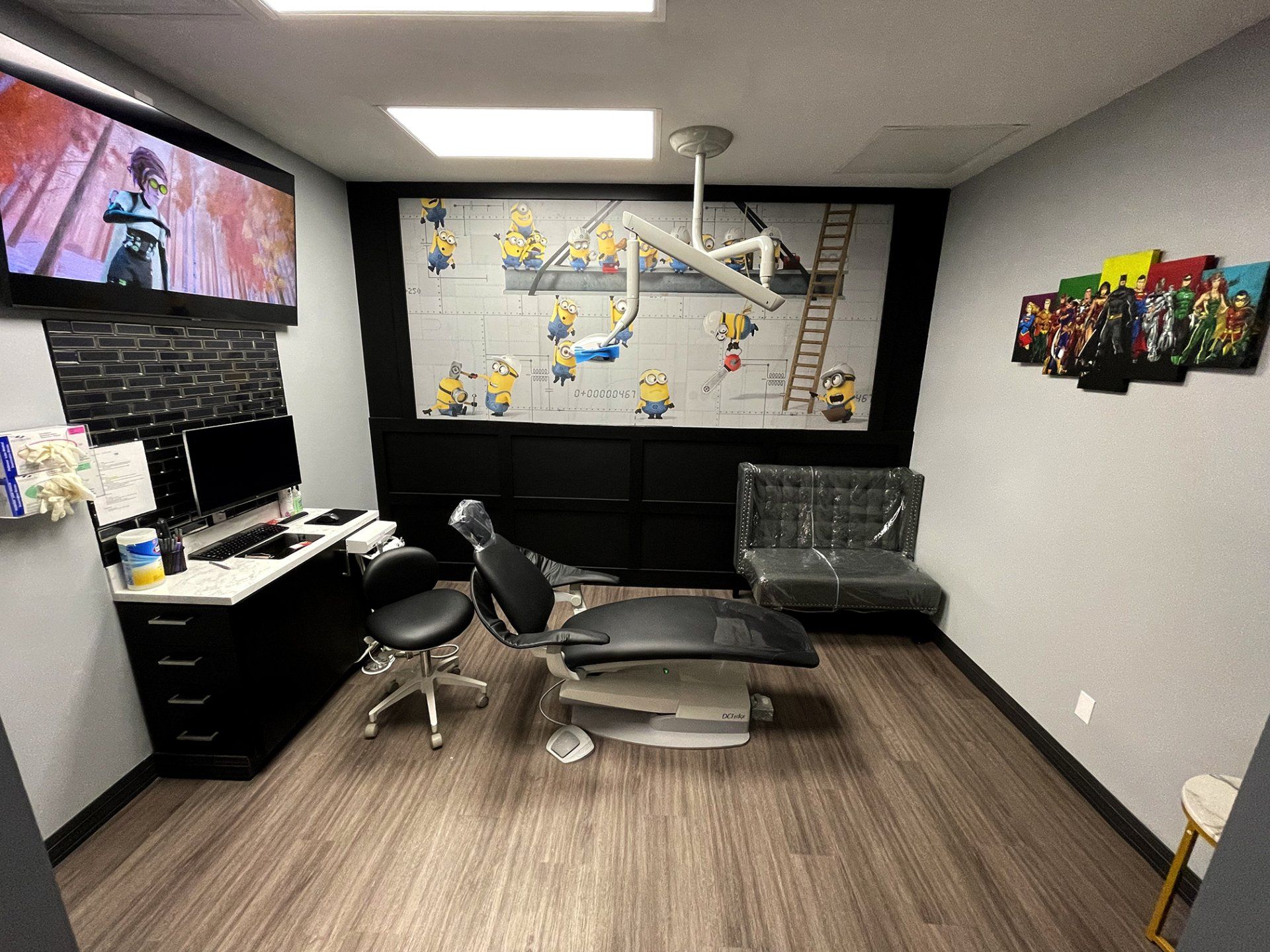 Home office with desk, monitors, black chair, wall art, and a gray sofa in a modern room.