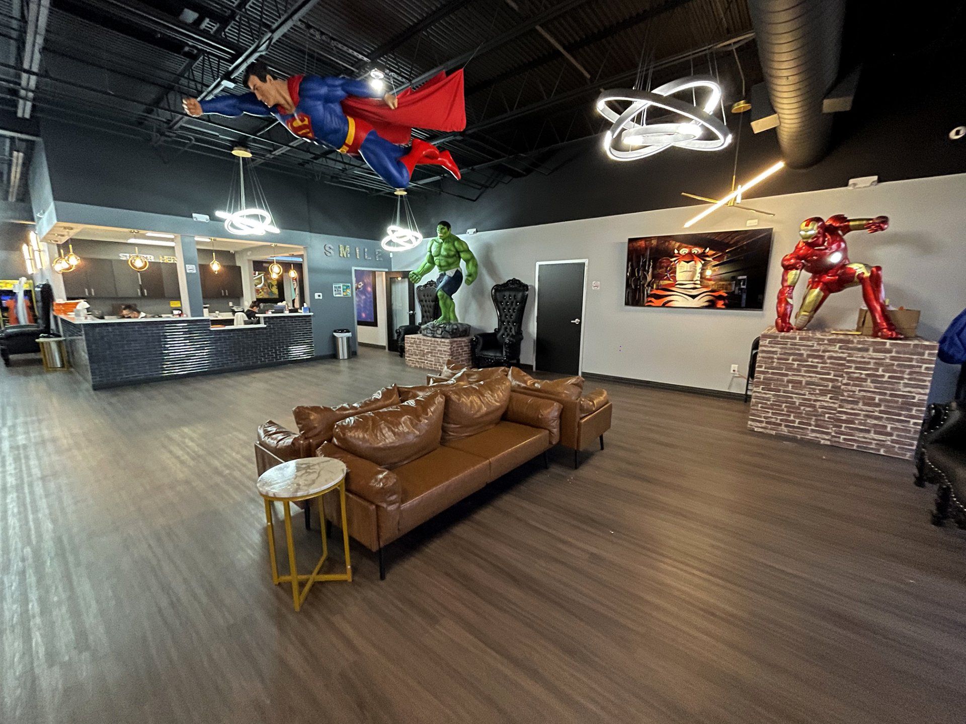 Modern office lobby with brown leather sofas, glowing ceiling lights, and a red superhero statue display