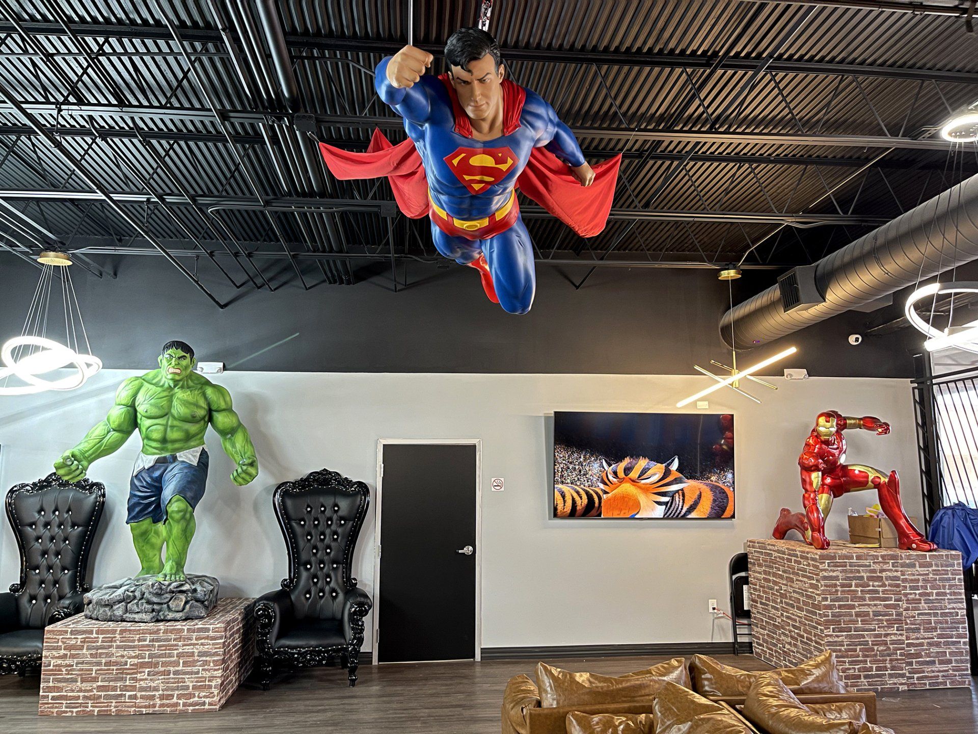 Superhero-themed room with Hulk and Iron Man statues and a hanging Superman figure in a white interior