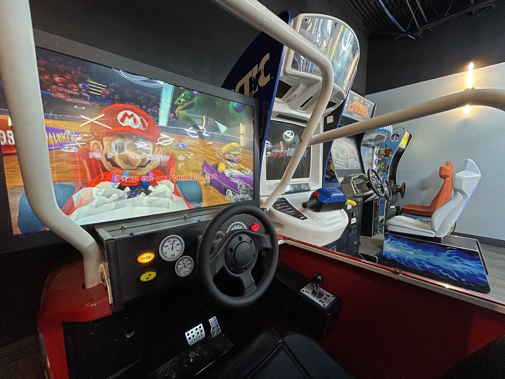 Mario Kart arcade racing game cabinet with steering wheel and colorful race screen, shown in an arcade booth