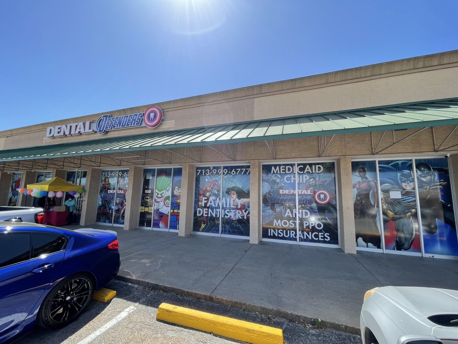 Strip mall storefronts with a dental office, parked cars, and bright sun overhead