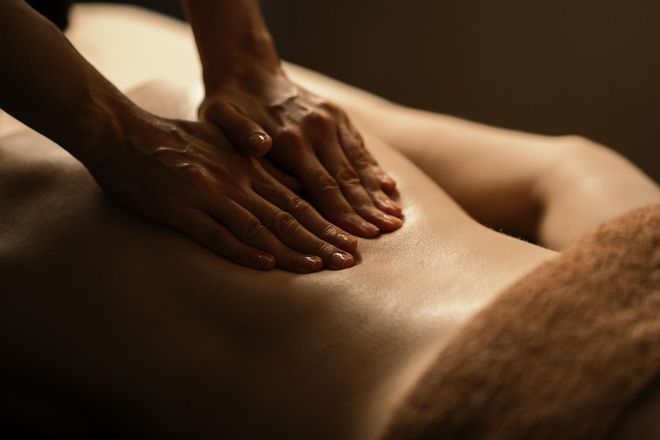Hands massaging a person's bare back in warm, dim light